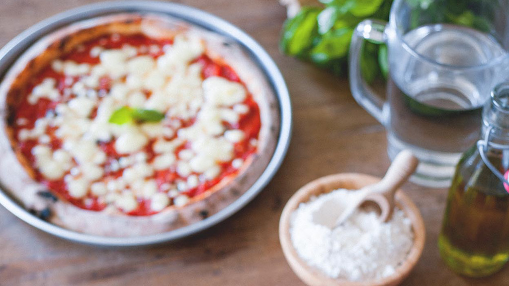 Pizza margherita appena sfornata con pomodoro, mozzarella a fiocchi e foglia di basilico
