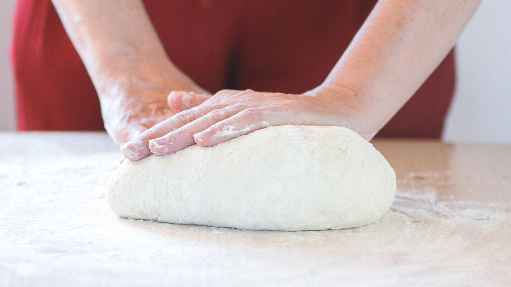 Mani che lavorano un panetto di impasto per pizza su piano infarinato