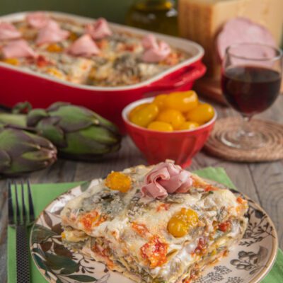 Lasagne con carciofi, mortadella e pomodorini gialli gratinate con parmigiano, servite a fetta