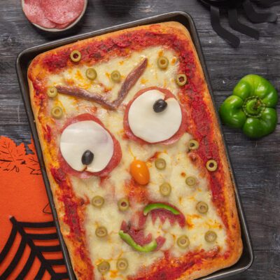 Pizza mostruosa con occhi di mozzarella e salame, olive e peperone a formare un volto spaventoso