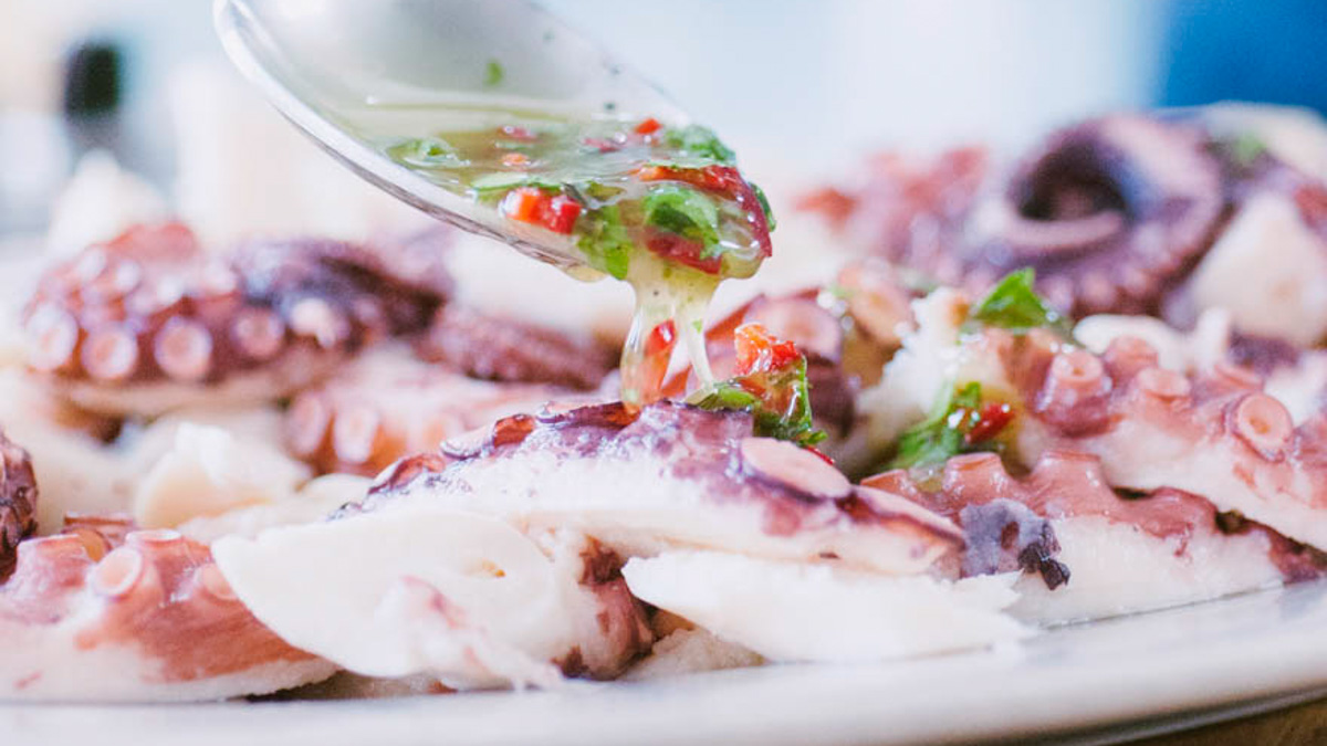 Emulsione con peperoncino e prezzemolo versata a cucchiaio sul polpo affettato