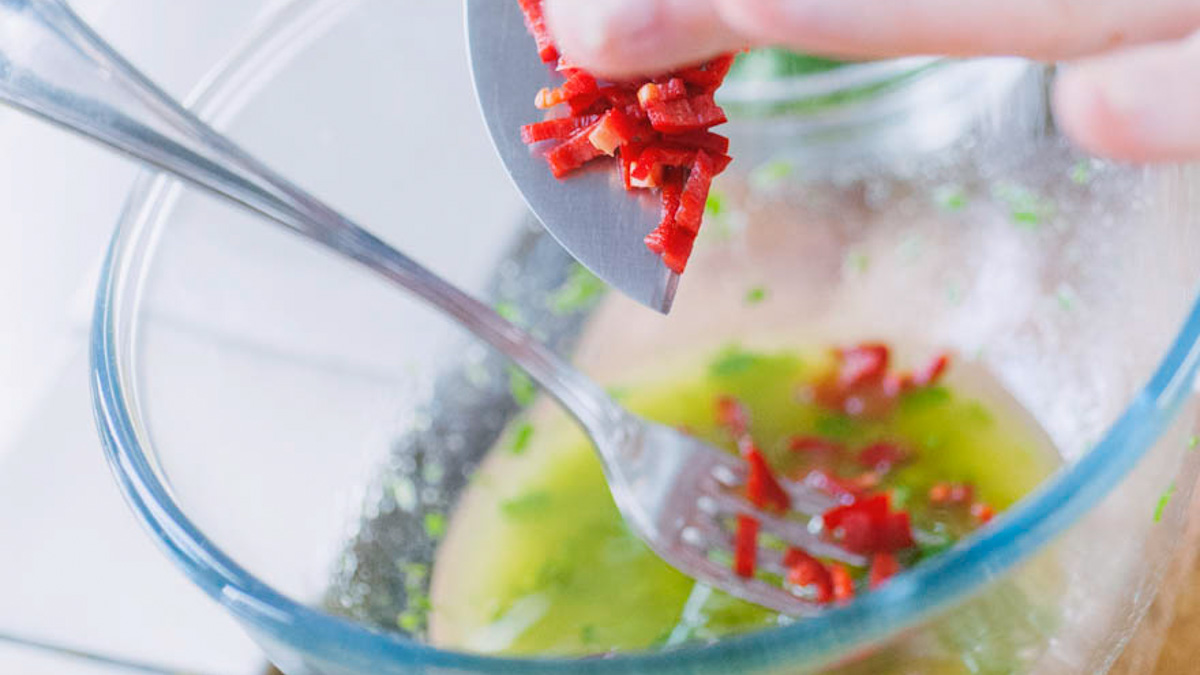 Peperoncino fresco tritato versato con un coltello in una ciotola con olio e prezzemolo