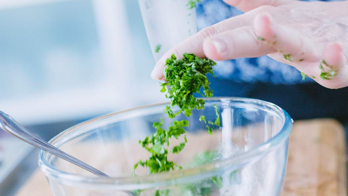 Mani che aggiungono prezzemolo tritato finemente in una ciotola con la vinaigrette