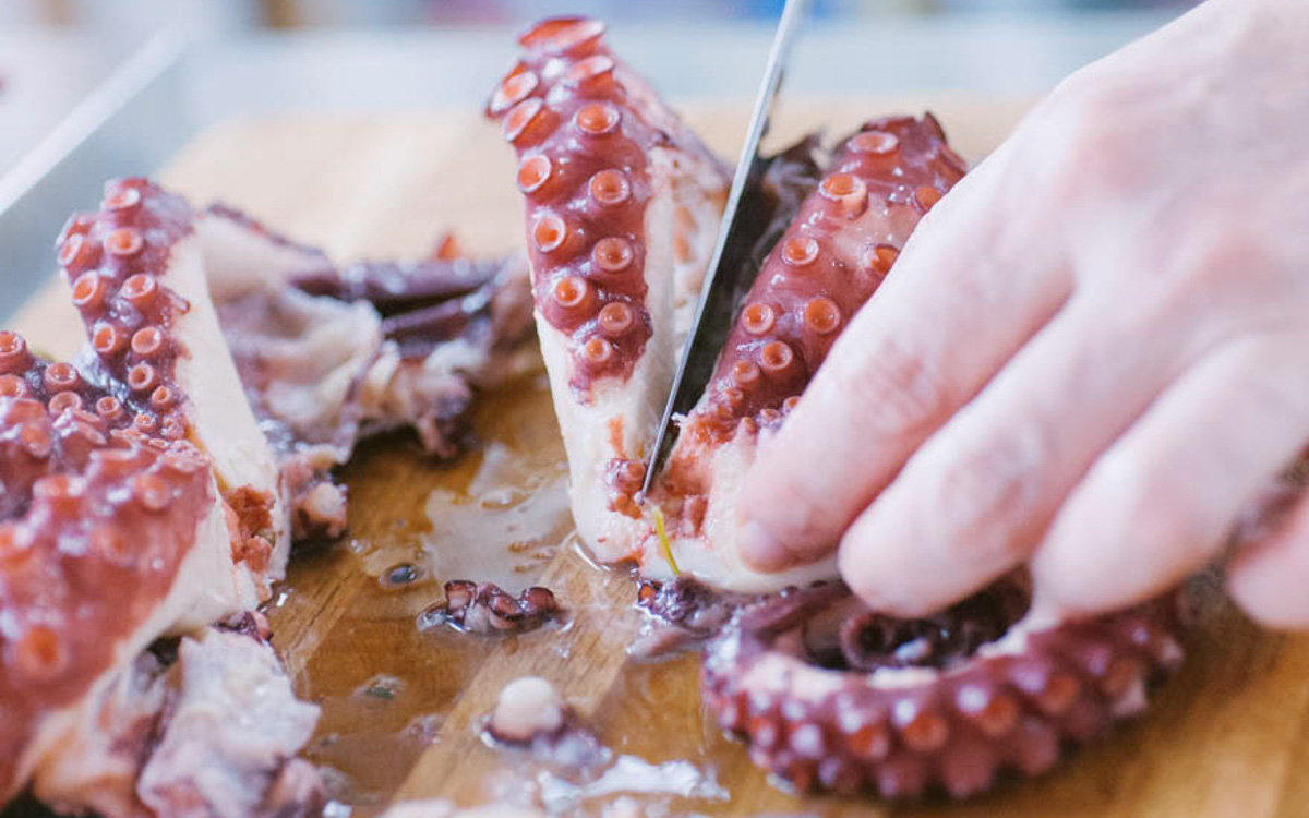 Mano che taglia a pezzi il polpo bollito sul tagliere, affettando i tentacoli con un coltello