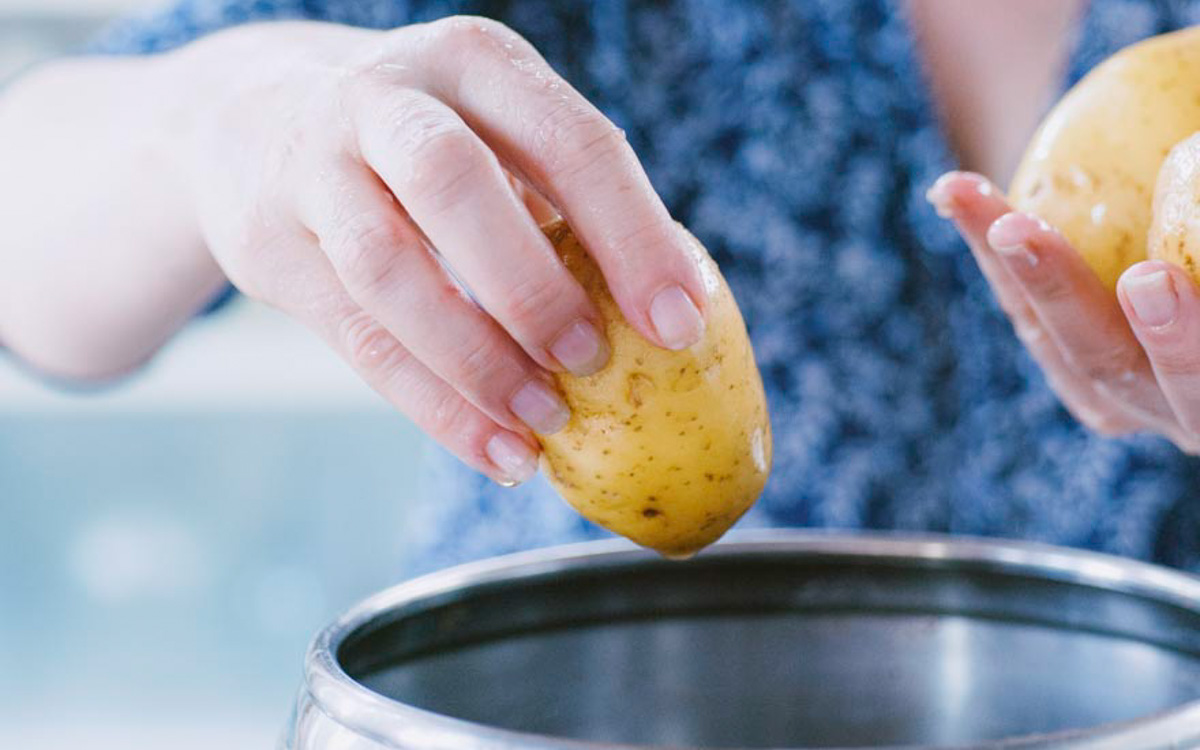 Mani che immergono patate con la buccia in una pentola d'acqua