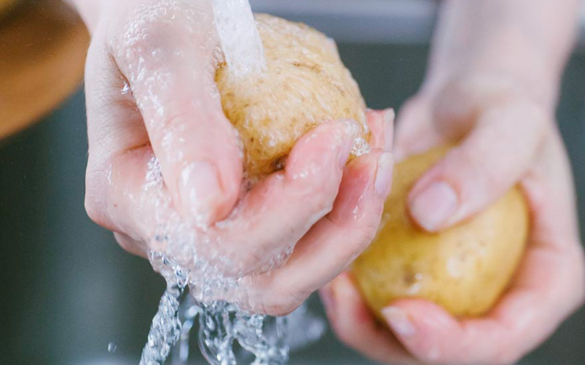 Mani che lavano una patata con la buccia sotto l'acqua corrente