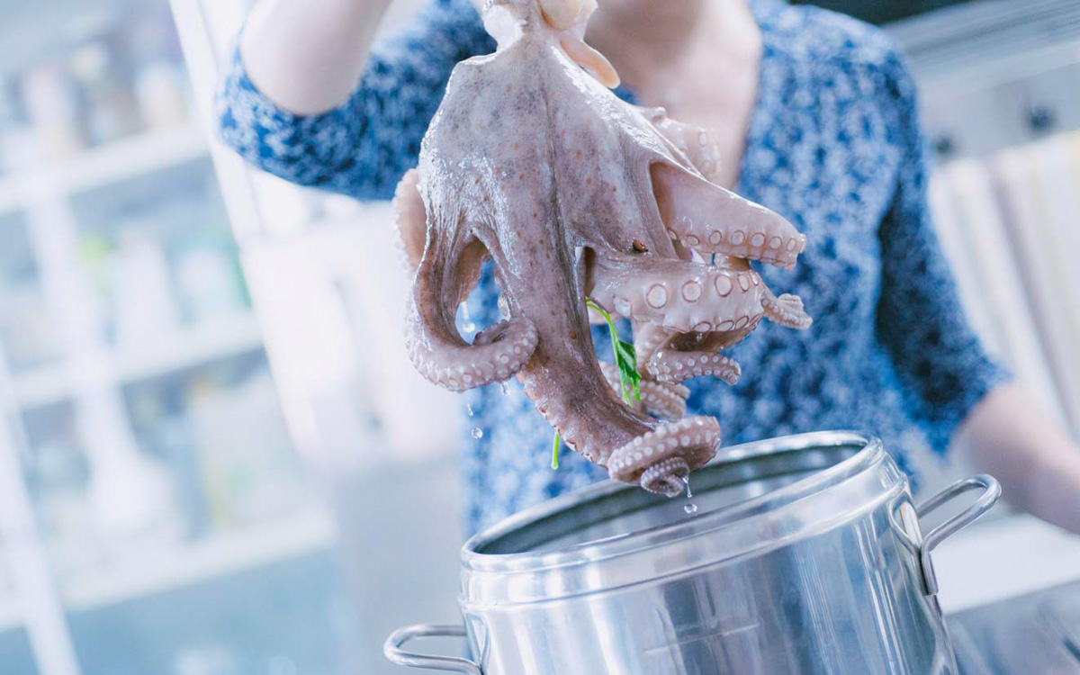 Polpo crudo sorretto per la testa e immerso con i tentacoli nell'acqua bollente
