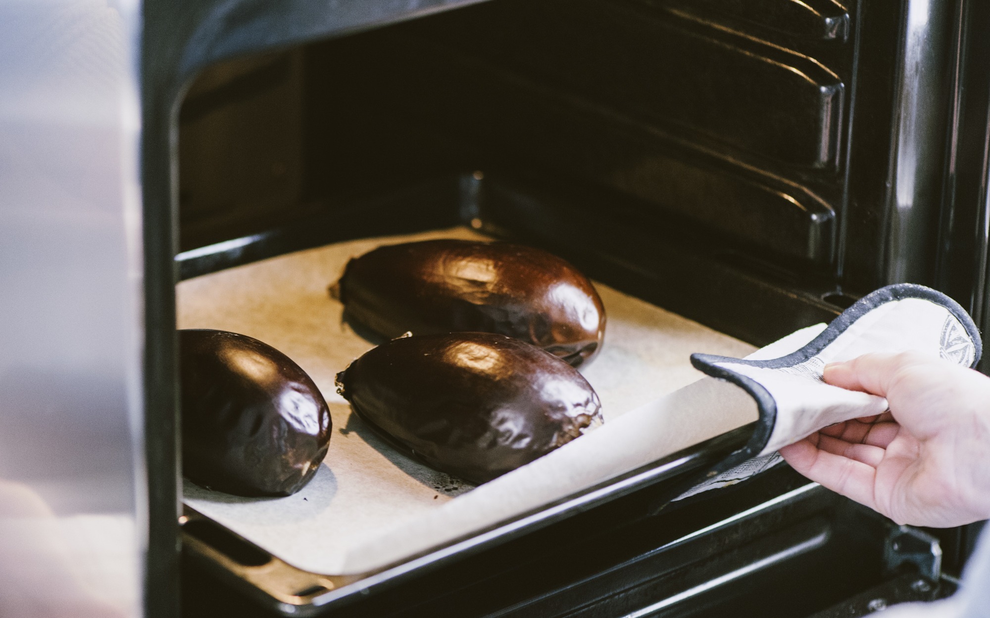 Melanzane intere in forno su carta forno, estratte con il guanto da forno