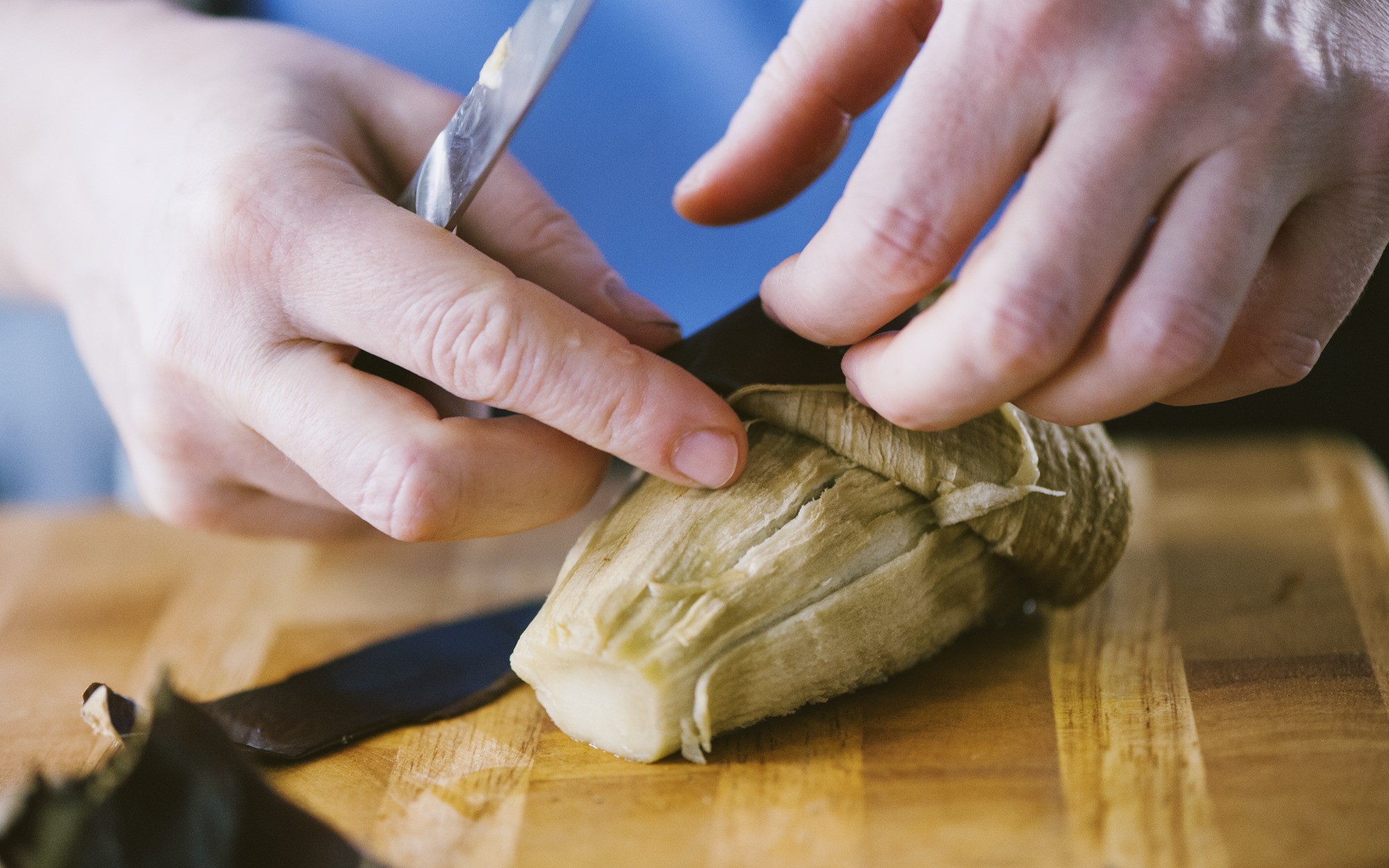 Mani che pelano una melanzana arrostita eliminando la buccia con un coltello