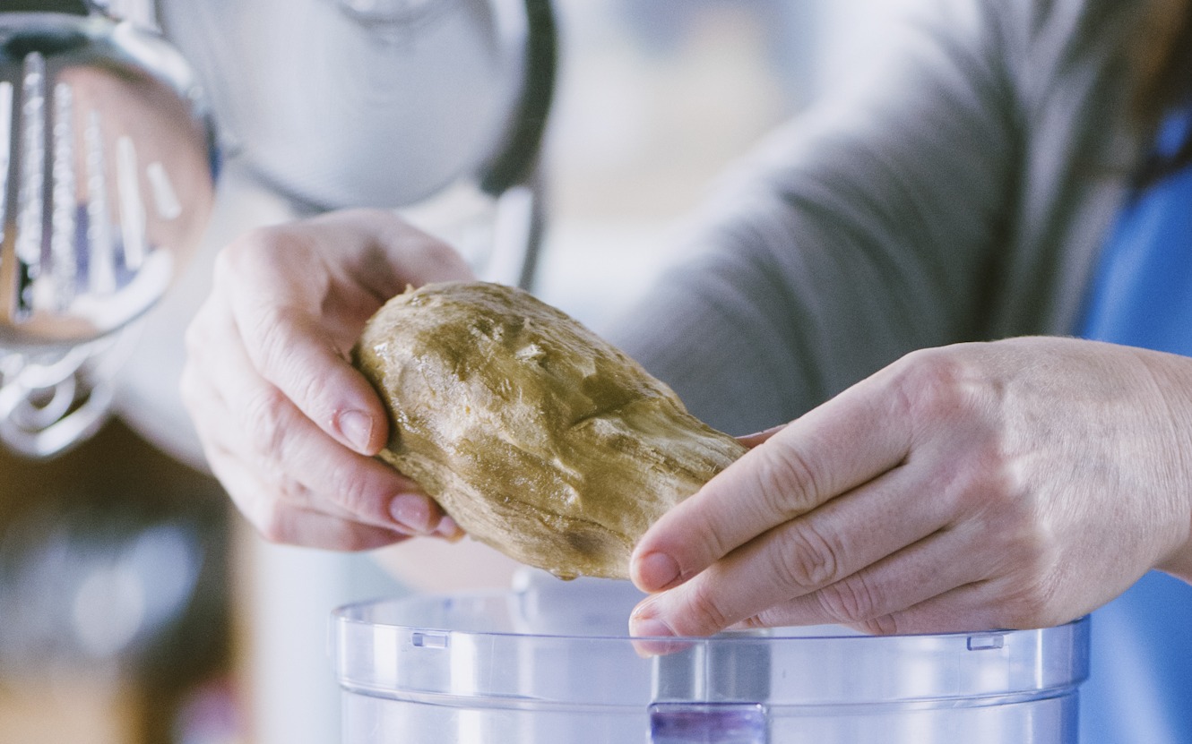 Mani che trasferiscono la polpa di melanzana scolata nel boccale del robot da cucina