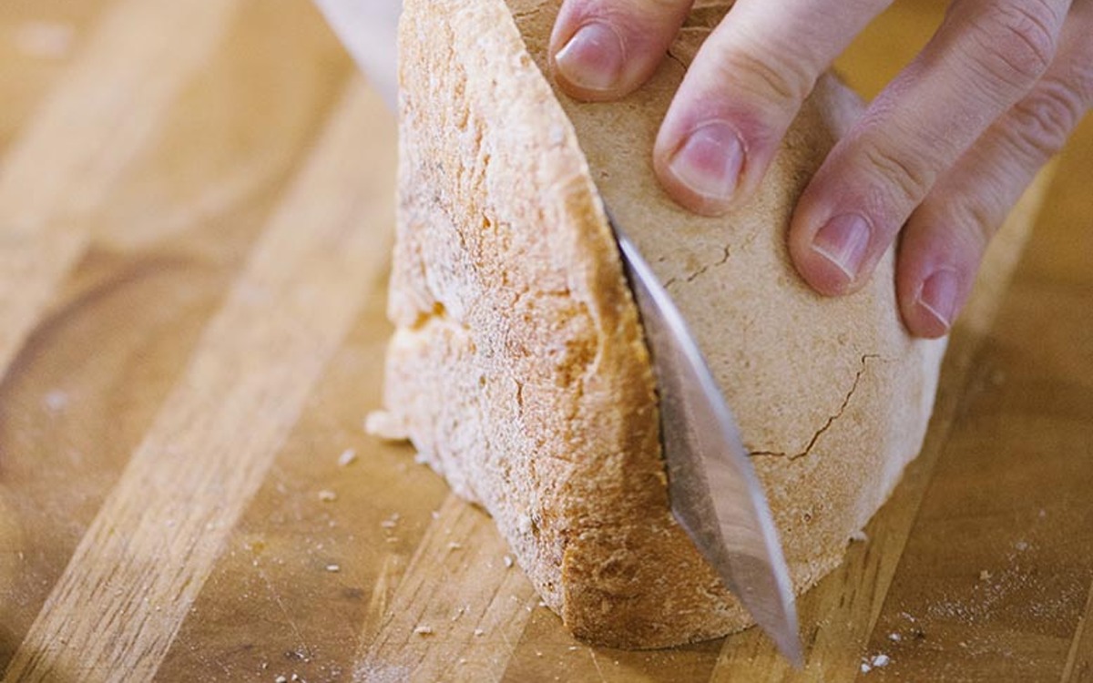 Una mano affetta con un coltello una fetta di pane casereccio dalla crosta dorata