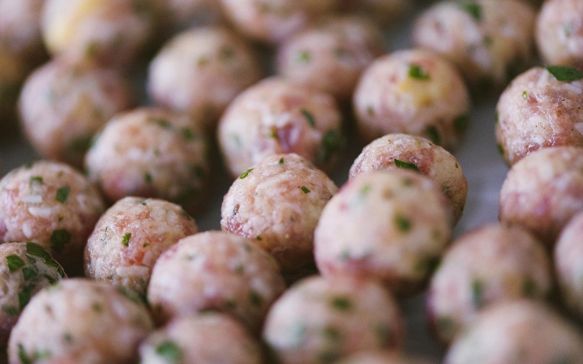 Polpette crude di carne con prezzemolo allineate in file ordinate, pronte per la cottura