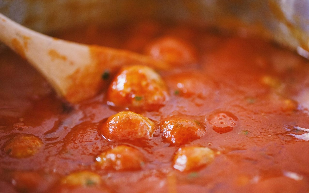 Polpette che sobbollono nel sugo di pomodoro, mescolate con un cucchiaio di legno