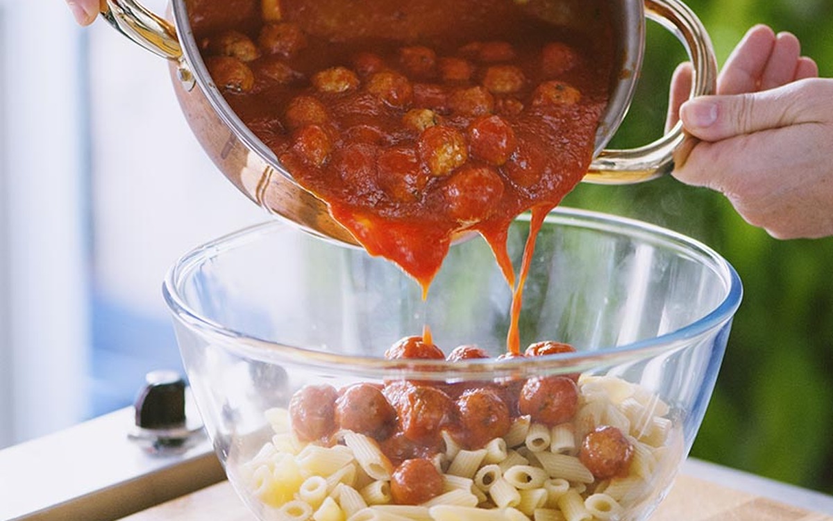 Sugo di pomodoro con polpette versato su rigatoni crudi in una ciotola
