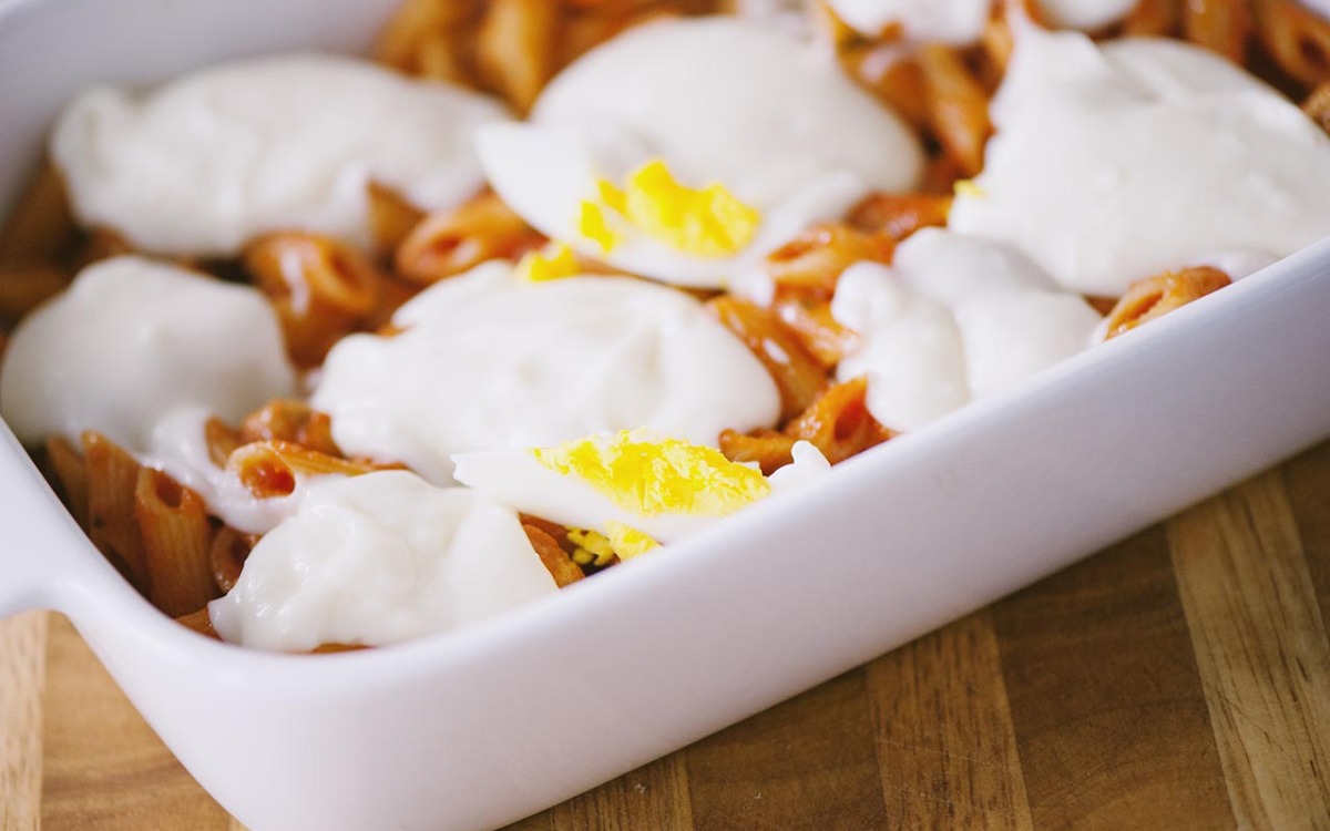 Pasta al forno con besciamella, uova sode tagliate e sugo di pomodoro nella teglia, pronta per il forno