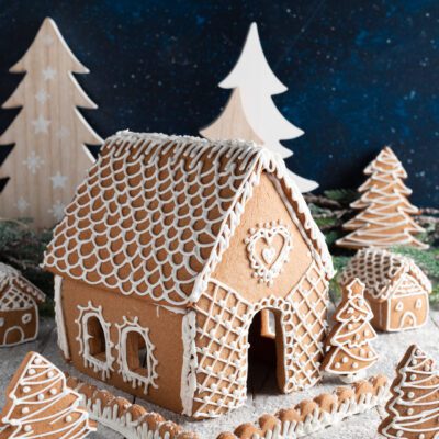 Casetta di pan di spezie decorata con glassa reale a motivi di tegole, cuori e alberelli natalizi