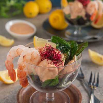 Cocktail di gamberi con salsa rosa, foglie verdi, germogli rossi e spicchio di limone