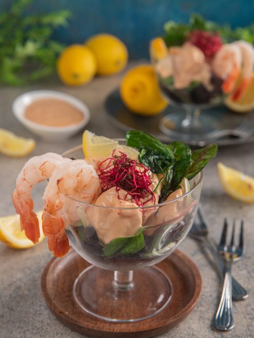 Cocktail di gamberi con salsa rosa, foglie verdi, germogli rossi e spicchio di limone
