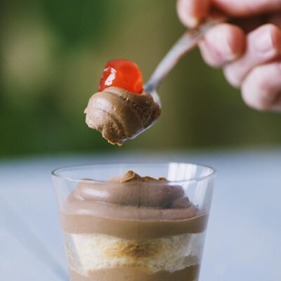 Crema al mascarpone al cioccolato a strati in bicchiere, con cucchiaiata guarnita da ciliegina candita