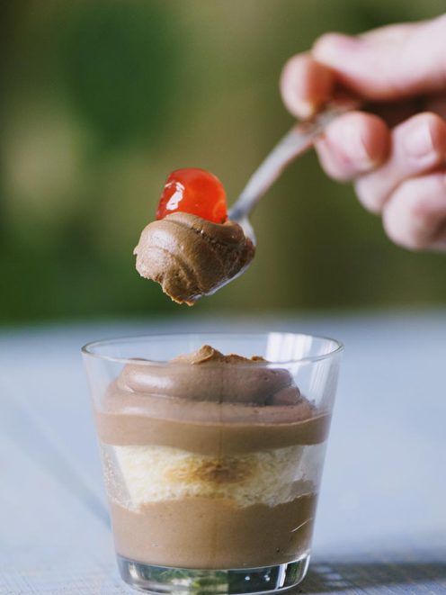 Crema al mascarpone al cioccolato a strati in bicchiere, con cucchiaiata guarnita da ciliegina candita