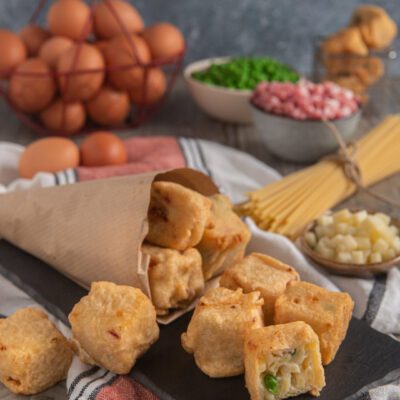 Frittatine di pasta alla napoletana fritte e dorate, una spezzata mostra il ripieno con piselli e prosciutto
