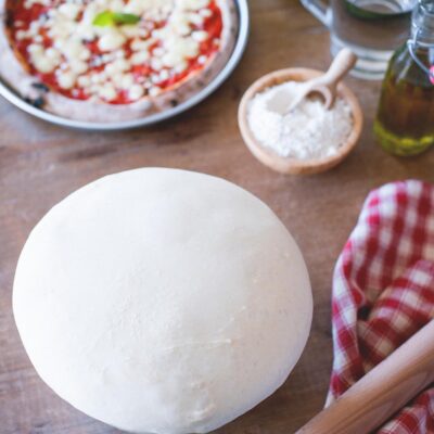 Impasto per pizza lievitato a palla, con pizza margherita al pomodoro e mozzarella sullo sfondo