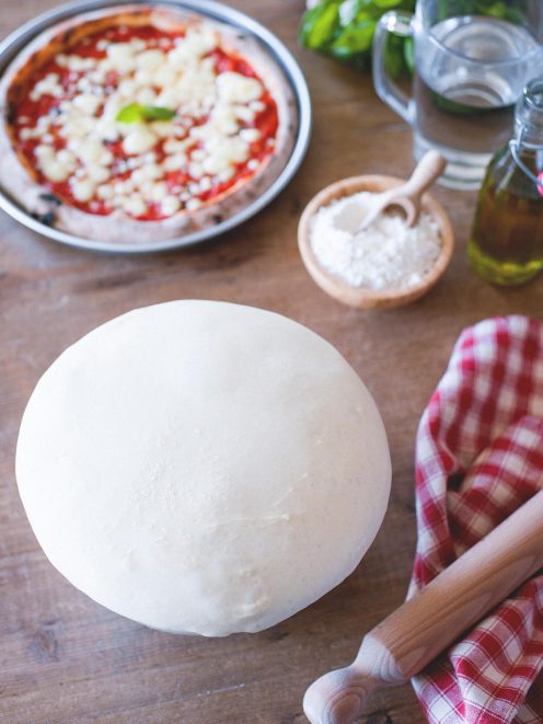 Impasto per pizza lievitato a palla, con pizza margherita al pomodoro e mozzarella sullo sfondo