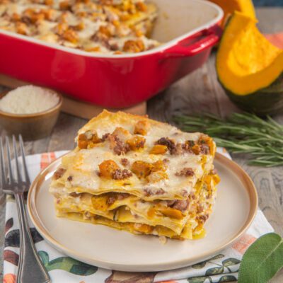 Lasagne con zucca e salsiccia servite a fetta, con besciamella filante e cubetti di zucca dorati