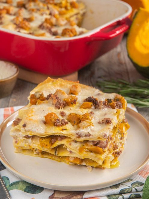 Lasagne con zucca e salsiccia servite a fetta, con besciamella filante e cubetti di zucca dorati