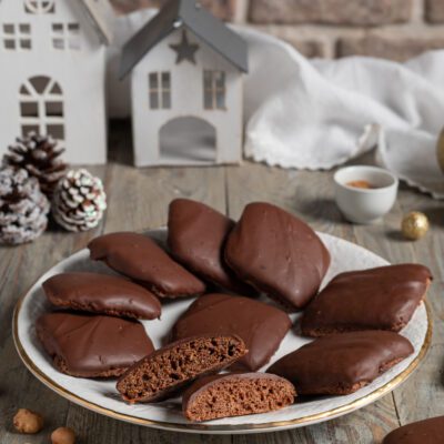 Mostaccioli napoletani ricoperti di glassa al cioccolato, uno spezzato mostra l'interno soffice, con mandorle e nocciole intorno