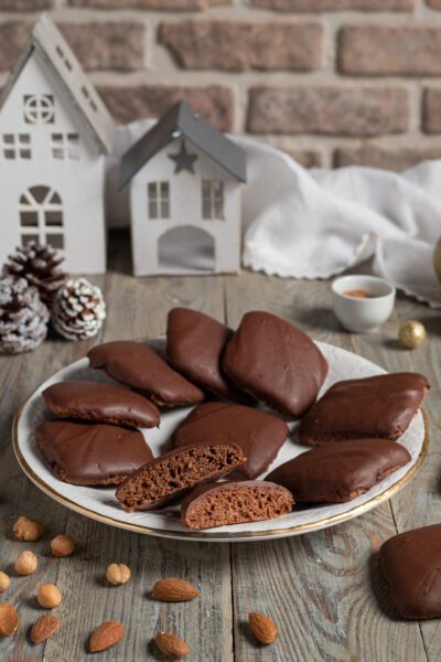 Mostaccioli napoletani ricoperti di glassa al cioccolato, uno spezzato mostra l'interno soffice, con mandorle e nocciole intorno