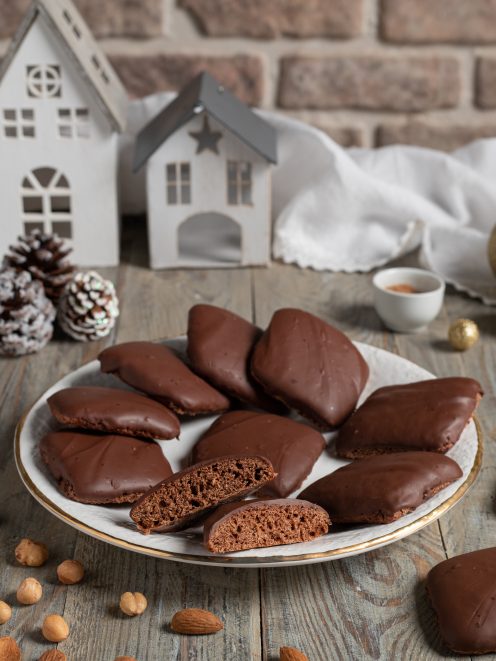 Mostaccioli napoletani ricoperti di glassa al cioccolato, uno spezzato mostra l'interno soffice, con mandorle e nocciole intorno