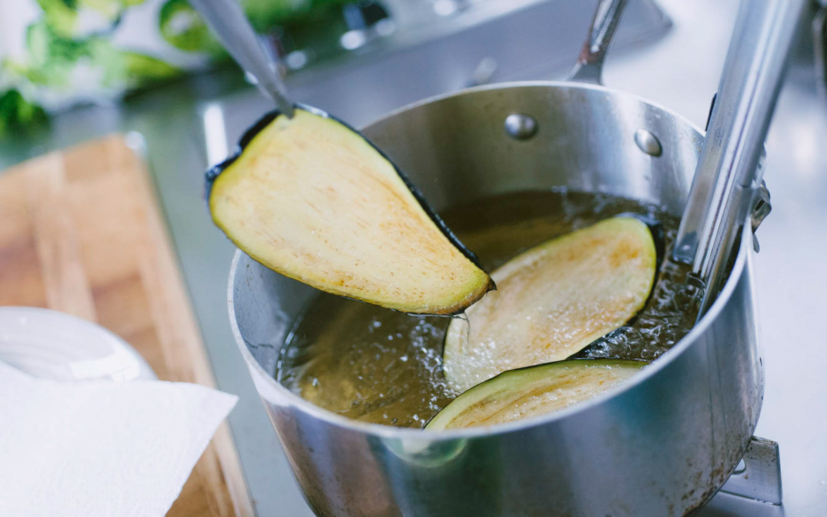 Fetta di melanzana sollevata dall'olio bollente con una spatola durante la frittura