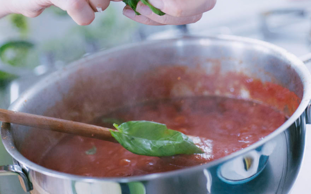 Foglie di basilico aggiunte a mano in un sugo di pomodoro in cottura