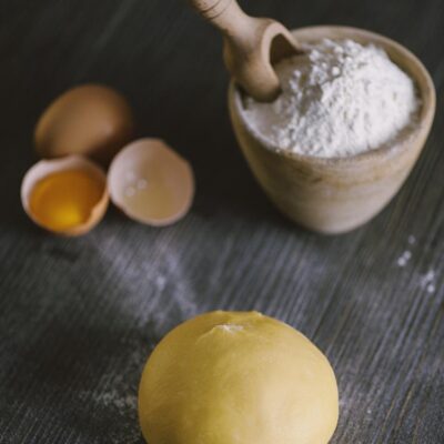 Pasta fresca all'uovo: palla di impasto giallo dorato con farina e uova aperte sullo sfondo
