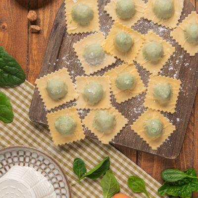 Ravioli ricotta e spinaci crudi disposti su tagliere infarinato, con il ripieno verde ben visibile