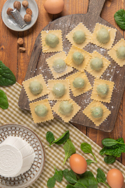 Ravioli ricotta e spinaci crudi disposti su tagliere infarinato, con il ripieno verde ben visibile