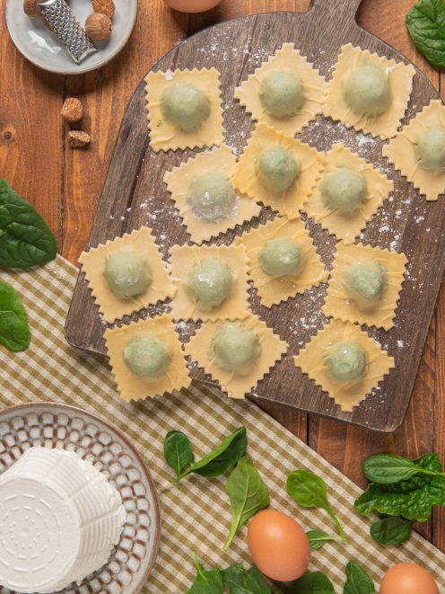 Ravioli ricotta e spinaci crudi disposti su tagliere infarinato, con il ripieno verde ben visibile