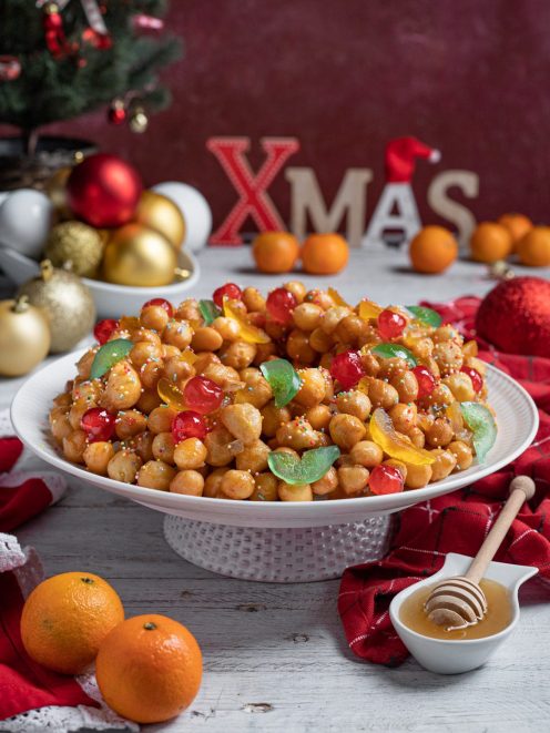 Struffoli glassati al miele con frutta candita colorata e codette, disposti a corona
