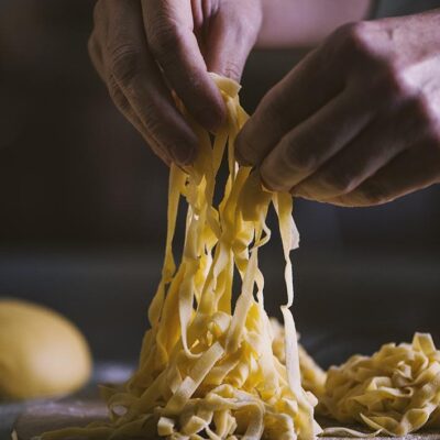 Tagliatelle all'uovo fresche sollevate a mano su un tagliere infarinato