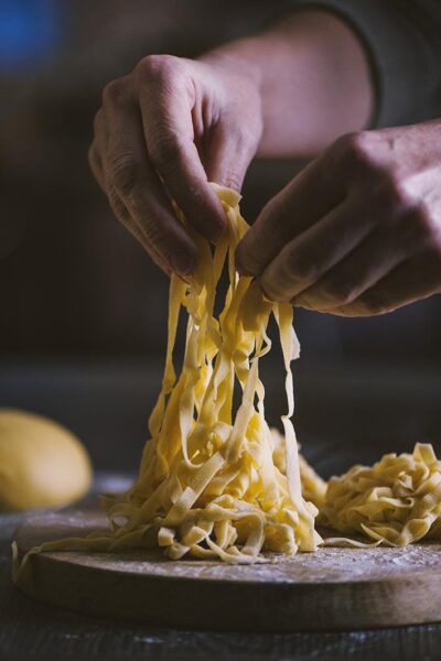 Tagliatelle all'uovo fresche sollevate a mano su un tagliere infarinato
