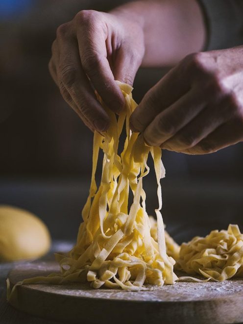 Tagliatelle all'uovo fresche sollevate a mano su un tagliere infarinato