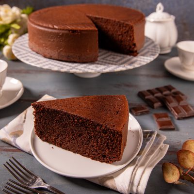 Torta al cioccolato con una fetta tagliata servita in primo piano, impasto soffice e scuro ben visibile