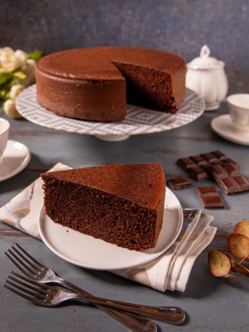 Torta al cioccolato con una fetta tagliata servita in primo piano, impasto soffice e scuro ben visibile