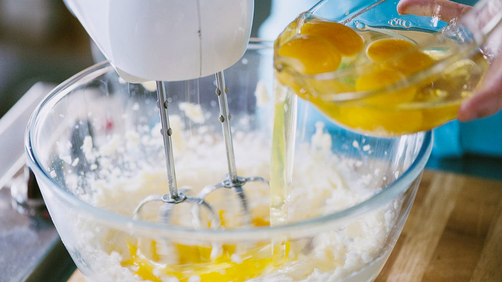Uova versate nel composto montato mentre le fruste elettriche lavorano l'impasto