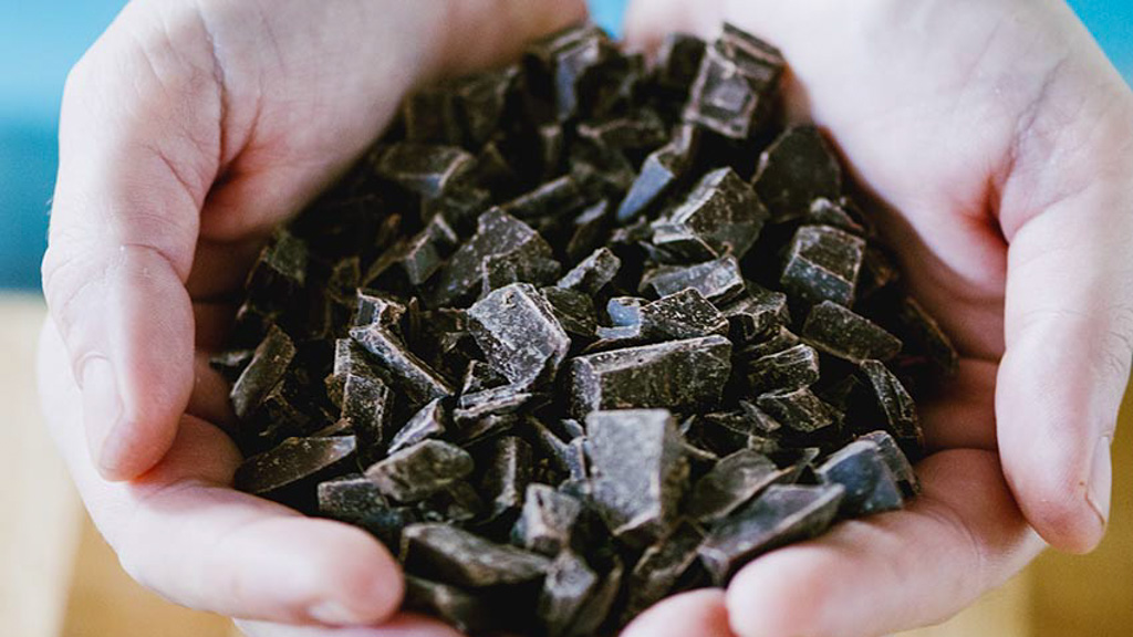 Mani che reggono pezzi di cioccolato fondente tritati grossolanamente