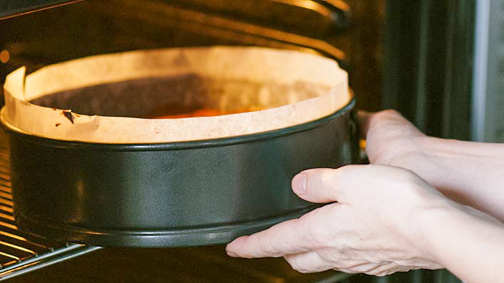 Teglia con carta forno infornata a mani nude per la cottura della torta al cioccolato