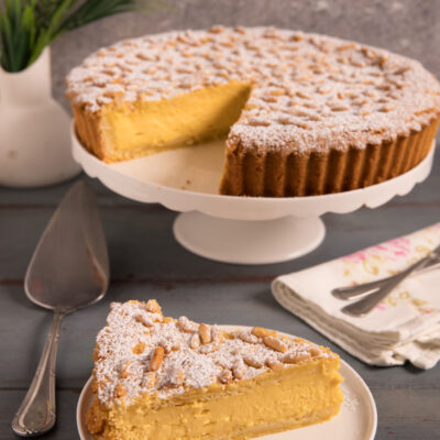 Torta della nonna con farcitura di crema pasticcera, pinoli e zucchero a velo, servita a fette