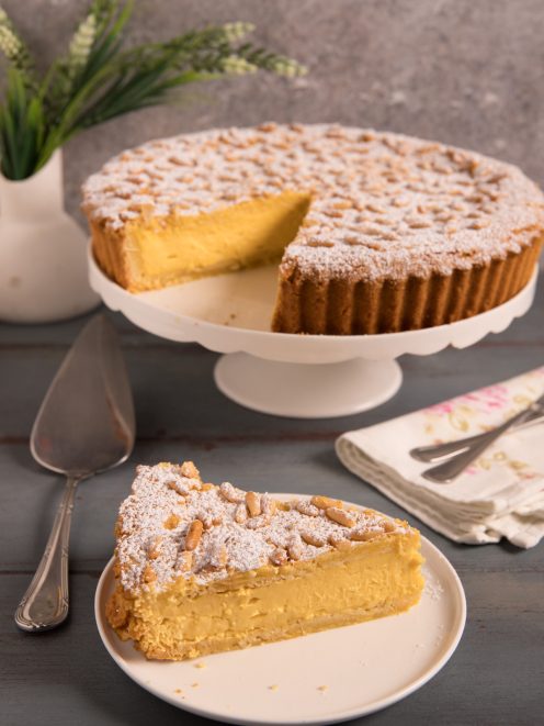 Torta della nonna con farcitura di crema pasticcera, pinoli e zucchero a velo, servita a fette