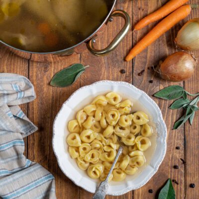 Tortellini in brodo serviti in un piatto fondo con brodo dorato e un cucchiaio